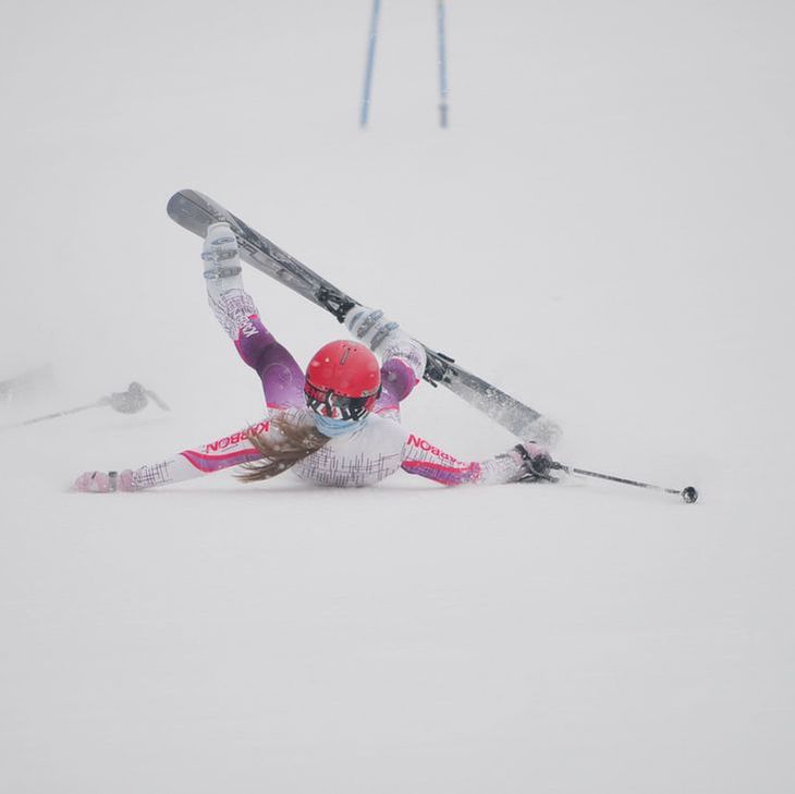 Picture of a young skier in white and purple racing gear who has fallen down in the snow.